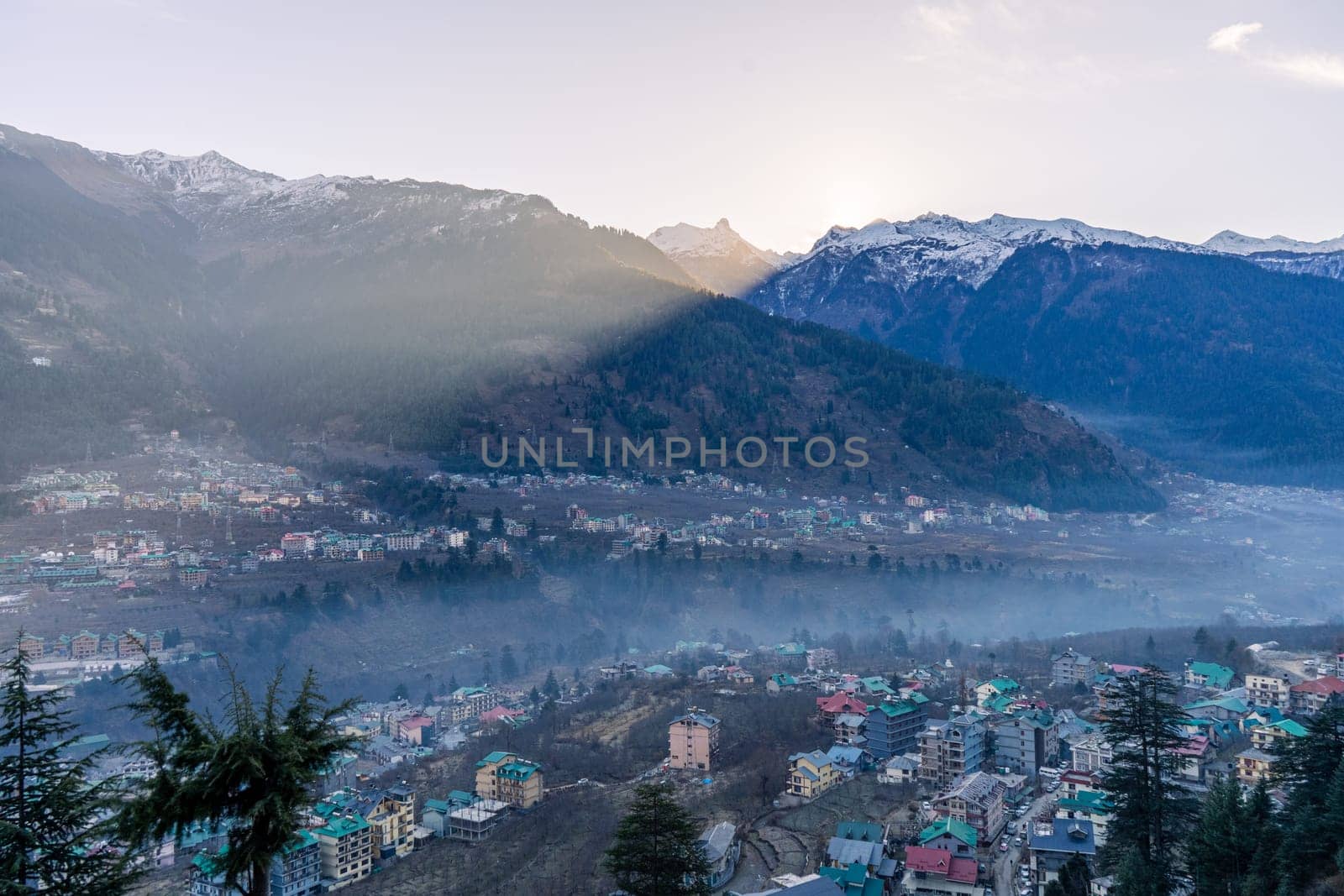 monsoon clouds moving over snow covered himalaya mountains with the blue orange sunset sunrise light with town of kullu manali valley at the base of mountains India