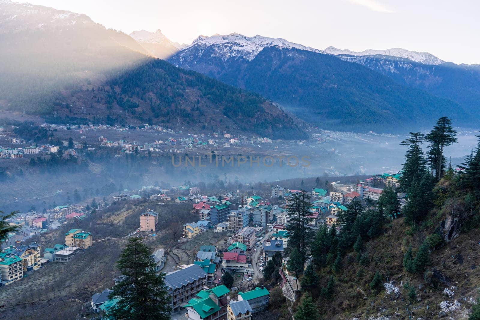 monsoon clouds moving over snow covered himalaya mountains with the blue orange sunset sunrise light with town of kullu manali valley at the base of mountains India
