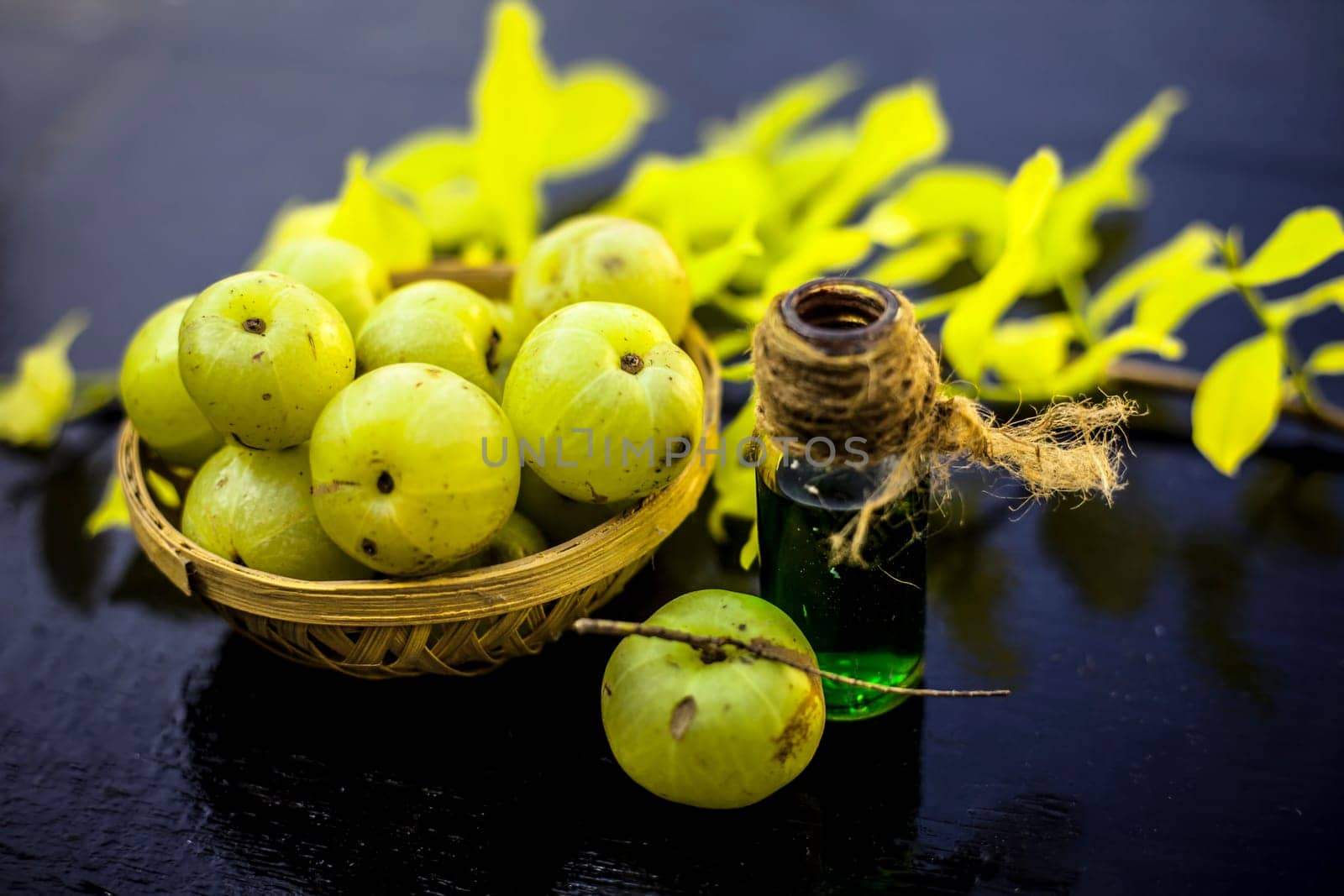 Close-up of Indian gooseberry with its extracted essence or concentration in a transparent bottle on a wooden surface with raw amla in a fruit and vegetable basket.