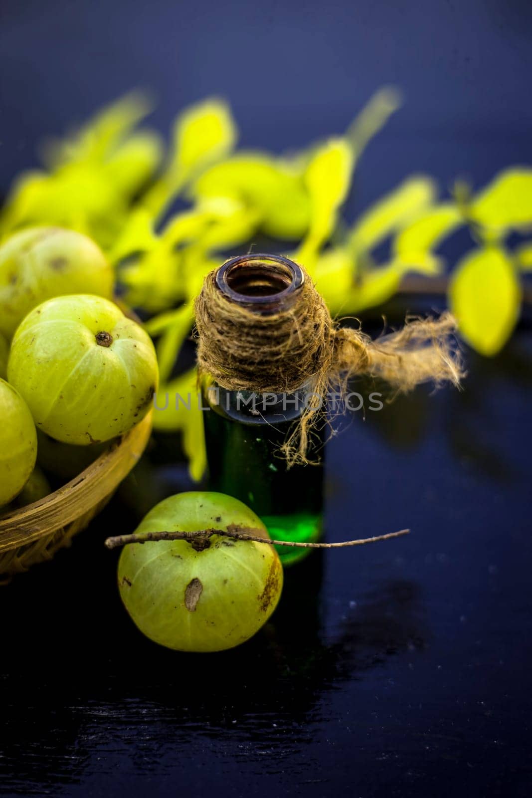 Close-up of Indian gooseberry with its extracted essence or concentration in a transparent bottle on a wooden surface with raw amla in a fruit and vegetable basket. by mirzamlk