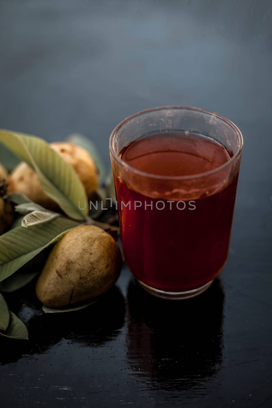 Close-up of organic juice of red guava or amarood or jamrukh in a transparent glass with raw guava and its leaves on the wooden surface. by mirzamlk