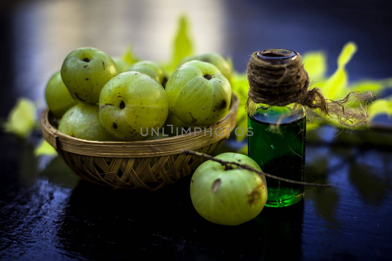 Close-up of Indian gooseberry with its extracted essence or concentration in a transparent bottle on a wooden surface with raw amla in a fruit and vegetable basket. by mirzamlk