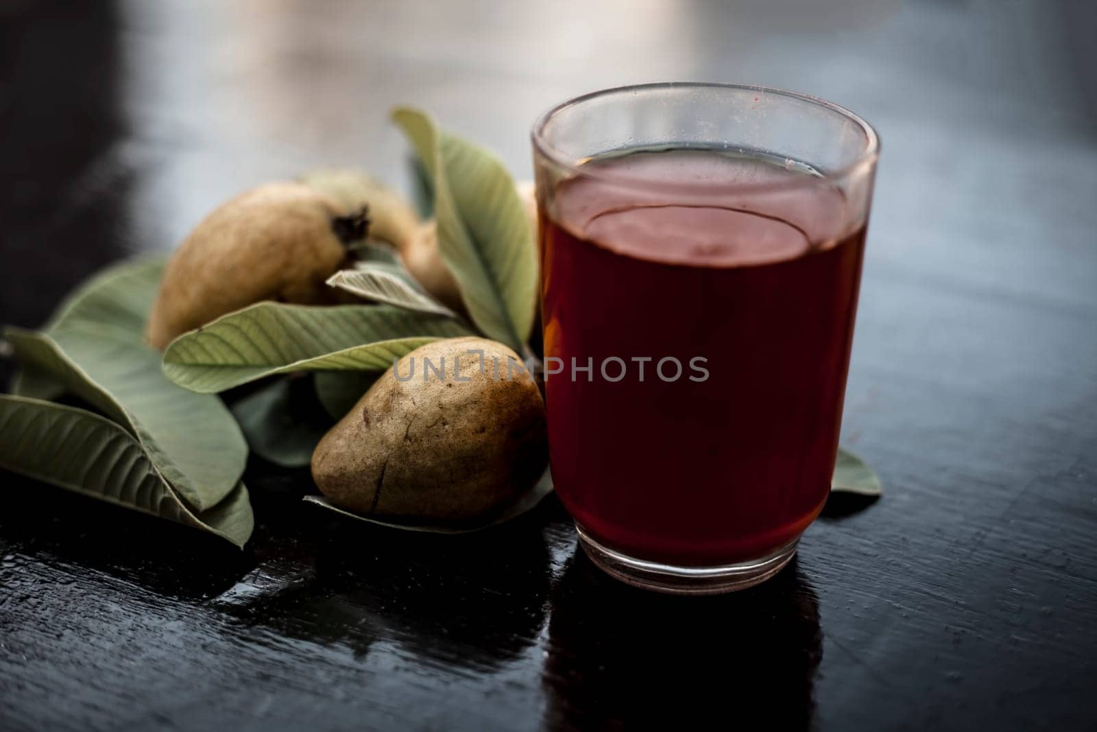 Close-up of organic juice of red guava or amarood or jamrukh in a transparent glass with raw guava and its leaves on the wooden surface. by mirzamlk