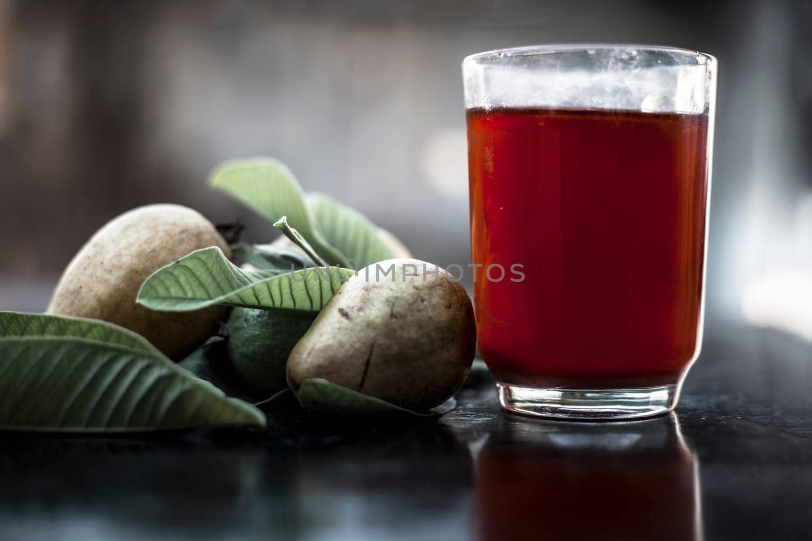 Close-up of organic juice of red guava or amarood or jamrukh in a transparent glass with raw guava and its leaves on the wooden surface.