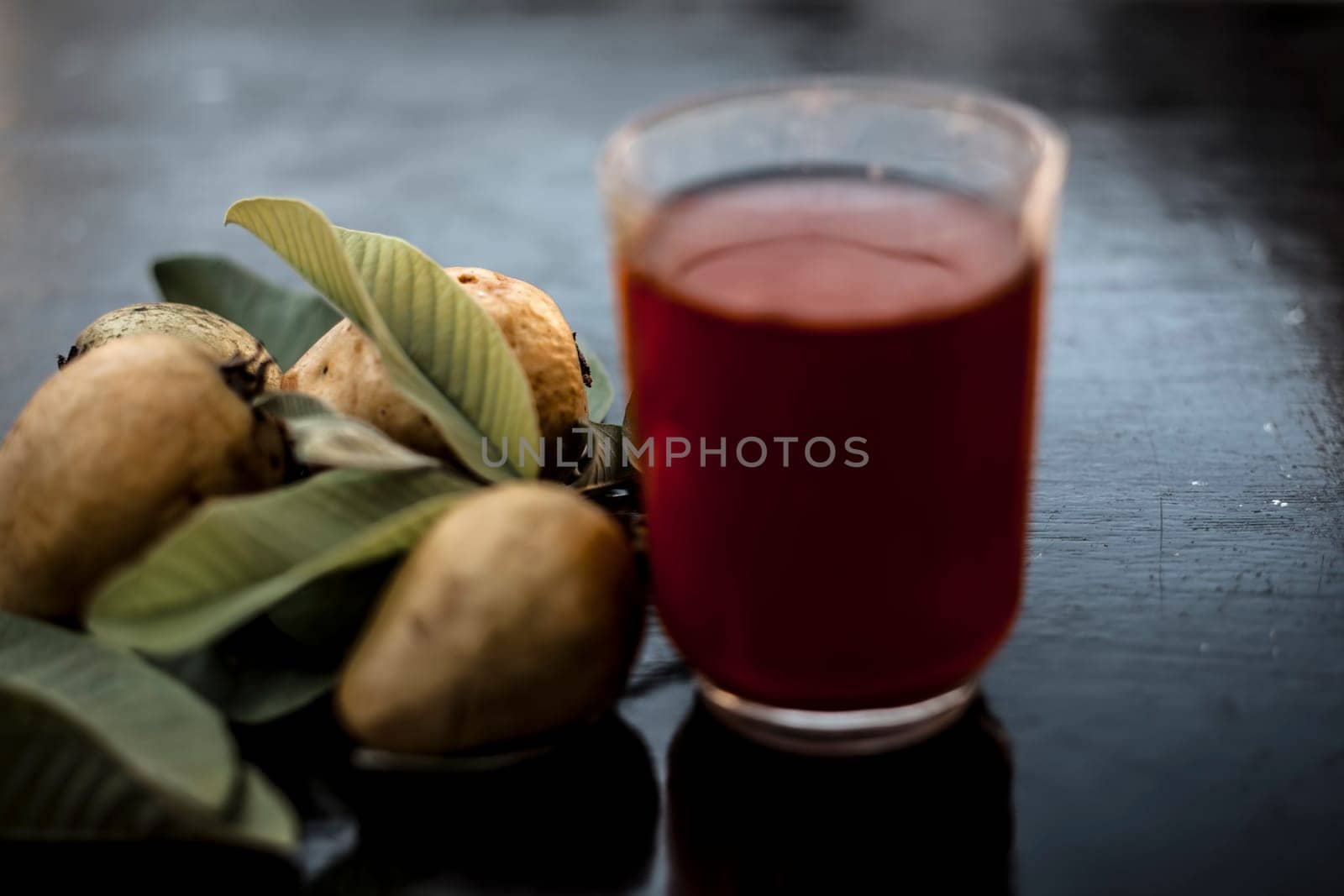 Close-up of organic juice of red guava or amarood or jamrukh in a transparent glass with raw guava and its leaves on the wooden surface. by mirzamlk
