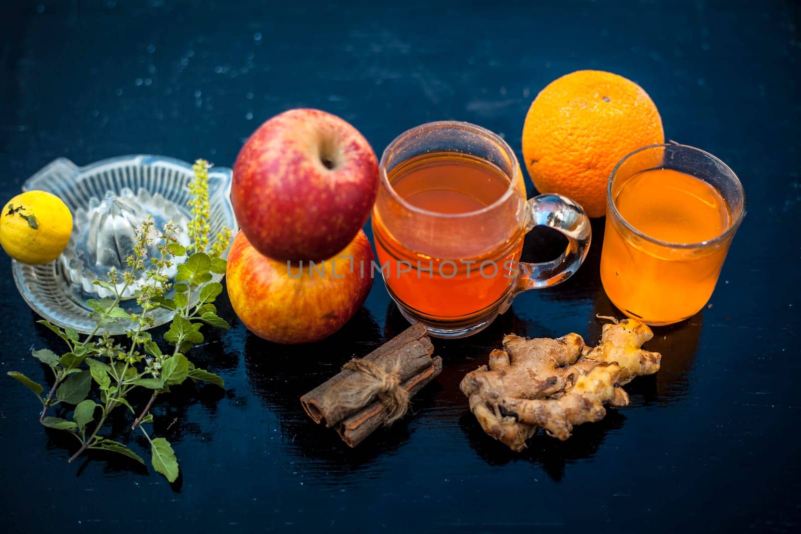 Close-up of herbal and organic juice of apple with orange juice, cinnamon sticks, lemon juice, ginger or adrak, and some tulsi leaves or holy basil leaves in a transparent glass with all raw ingredients. by mirzamlk