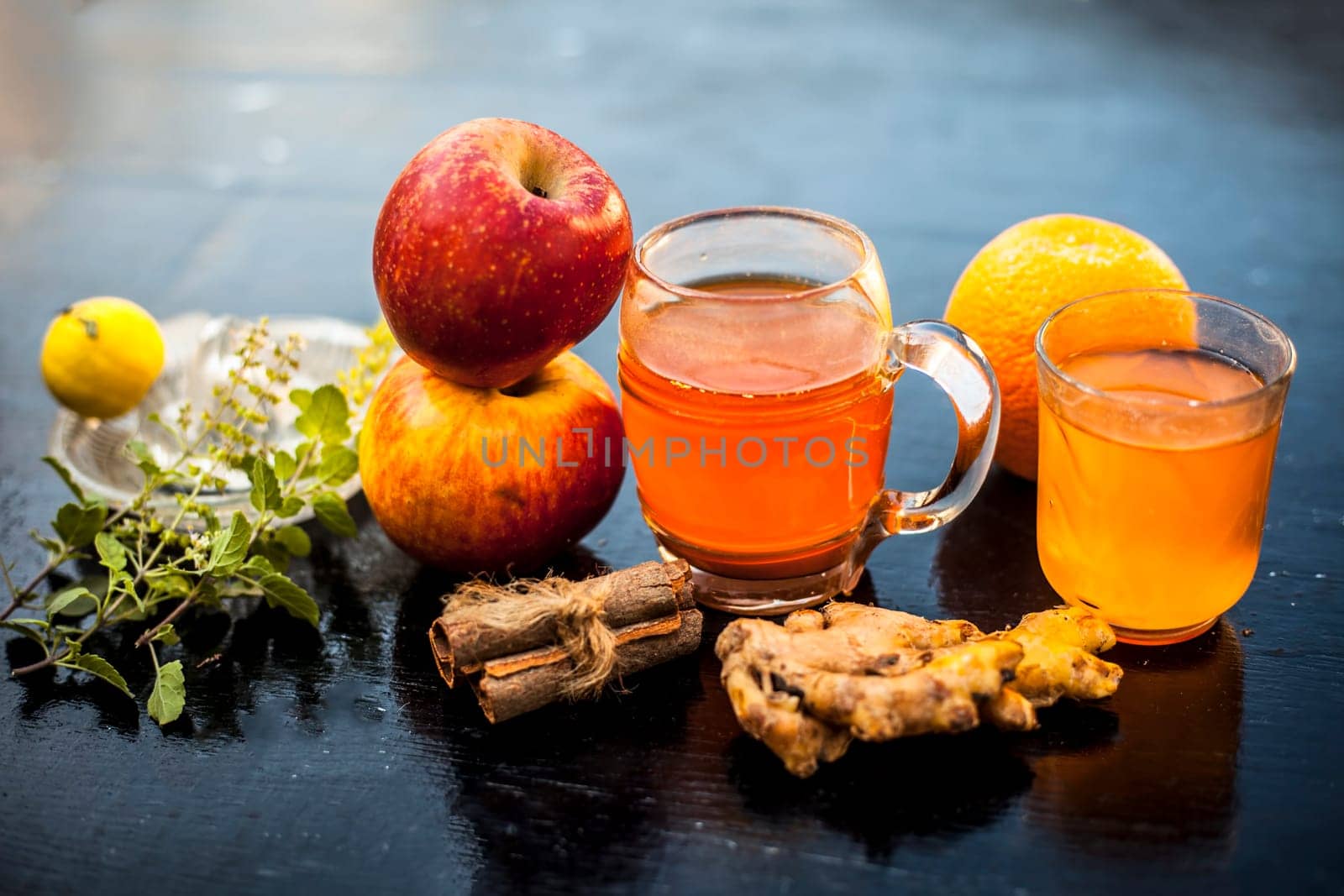 Close-up of herbal and organic juice of apple with orange juice, cinnamon sticks, lemon juice, ginger or adrak, and some tulsi leaves or holy basil leaves in a transparent glass with all raw ingredients. by mirzamlk