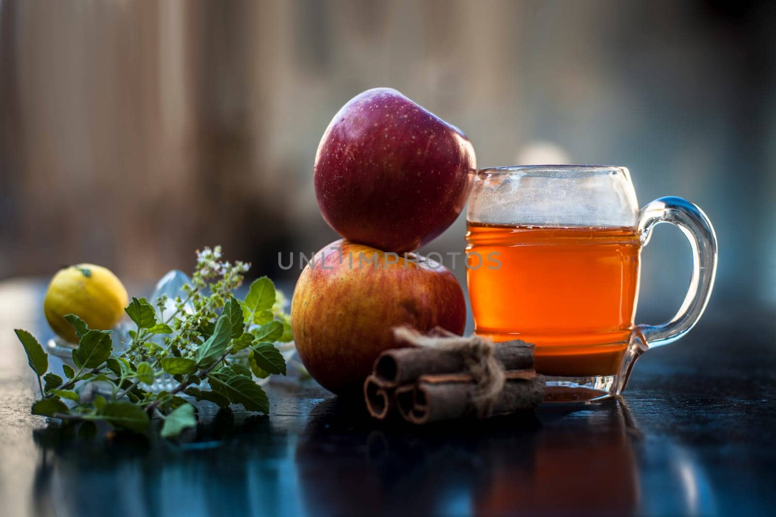 Close-up of herbal and organic juice of apple with orange juice, cinnamon sticks, lemon juice, ginger or adrak, and some tulsi leaves or holy basil leaves in a transparent glass with all raw ingredients. by mirzamlk