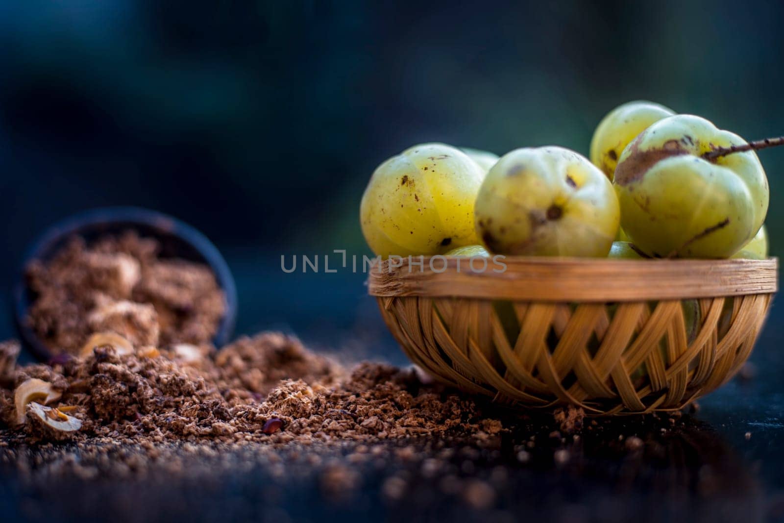 Close-up of raw amla or Phyllanthus emblica or Indian gooseberry in a fruit basket with its dried seed powder in a clay bowl used in a face pack, drinks, and natural medicines on the wooden surface. by mirzamlk