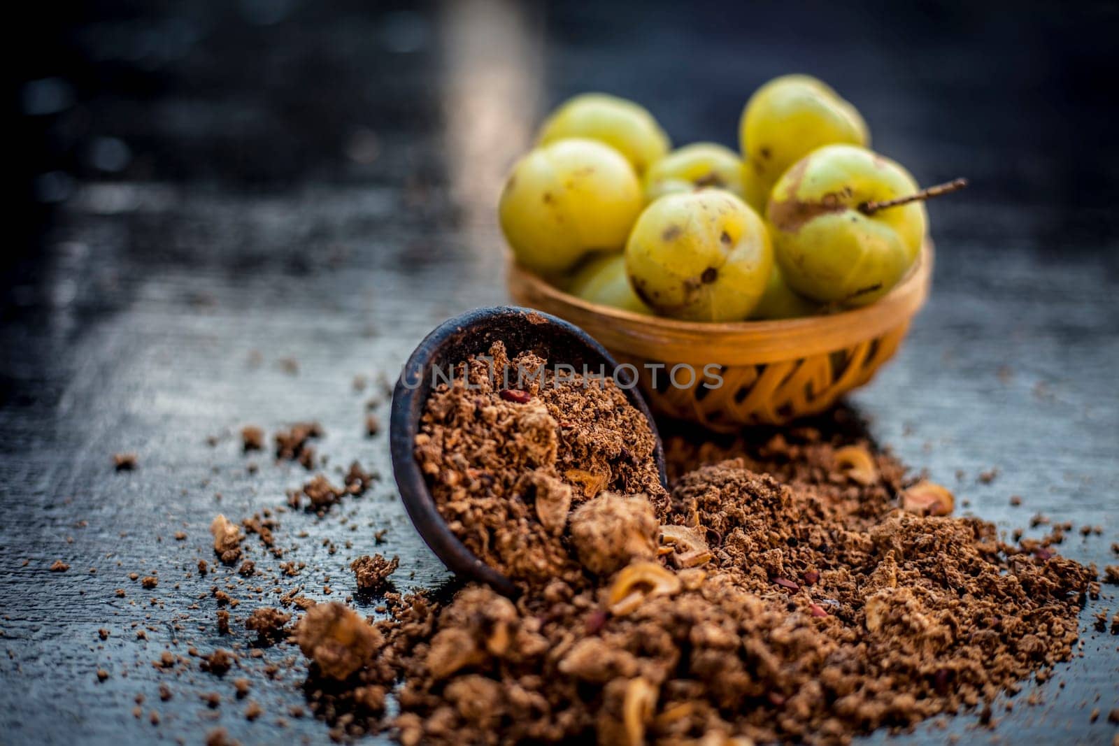 Close-up of raw amla or Phyllanthus emblica or Indian gooseberry in a fruit basket with its dried seed powder in a clay bowl used in a face pack, drinks, and natural medicines on the wooden surface. by mirzamlk