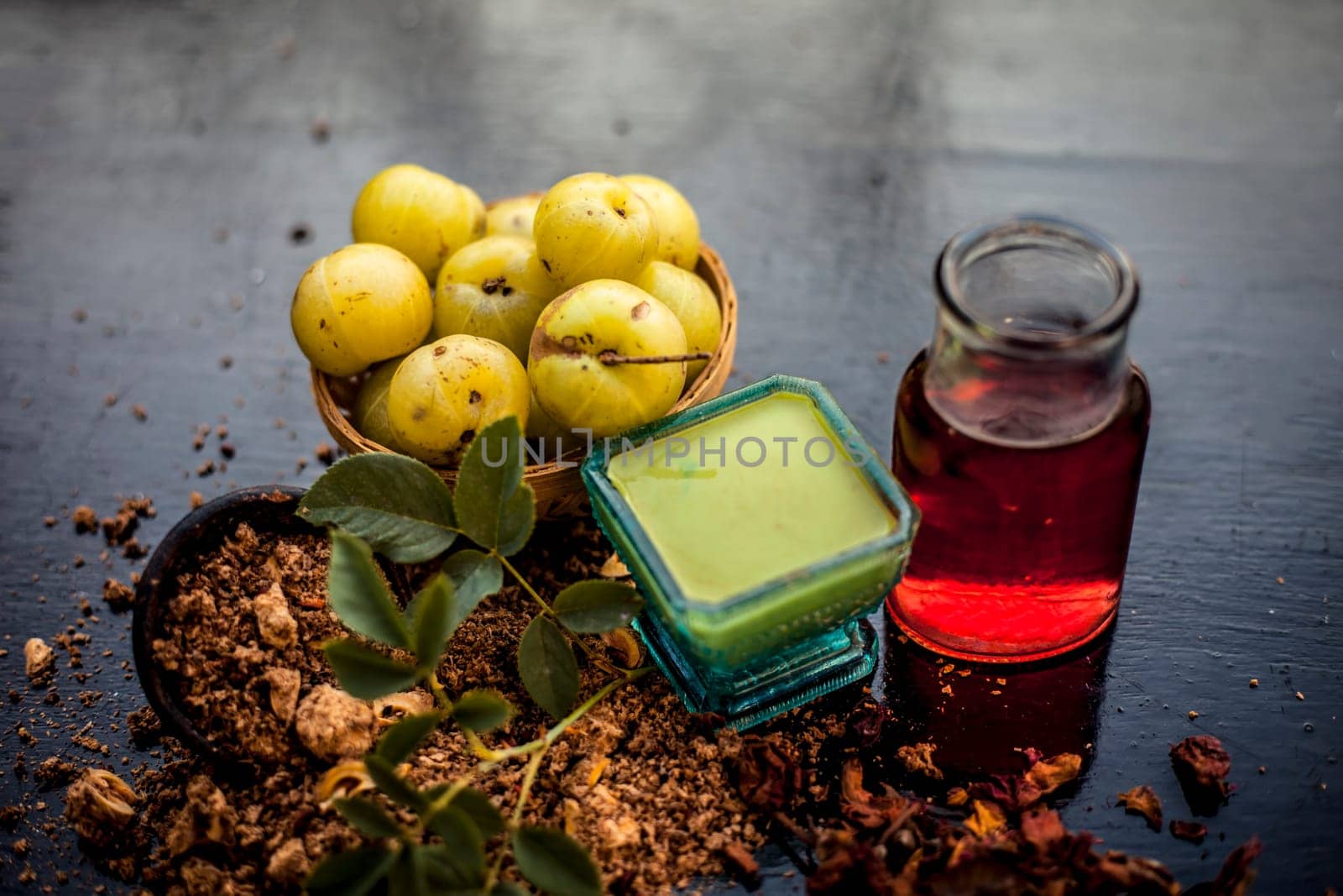 Close-up of ingredients of treatment for oily skin on a wooden surface i.e. amla powder with some raw organic rose water in a glass bowl.