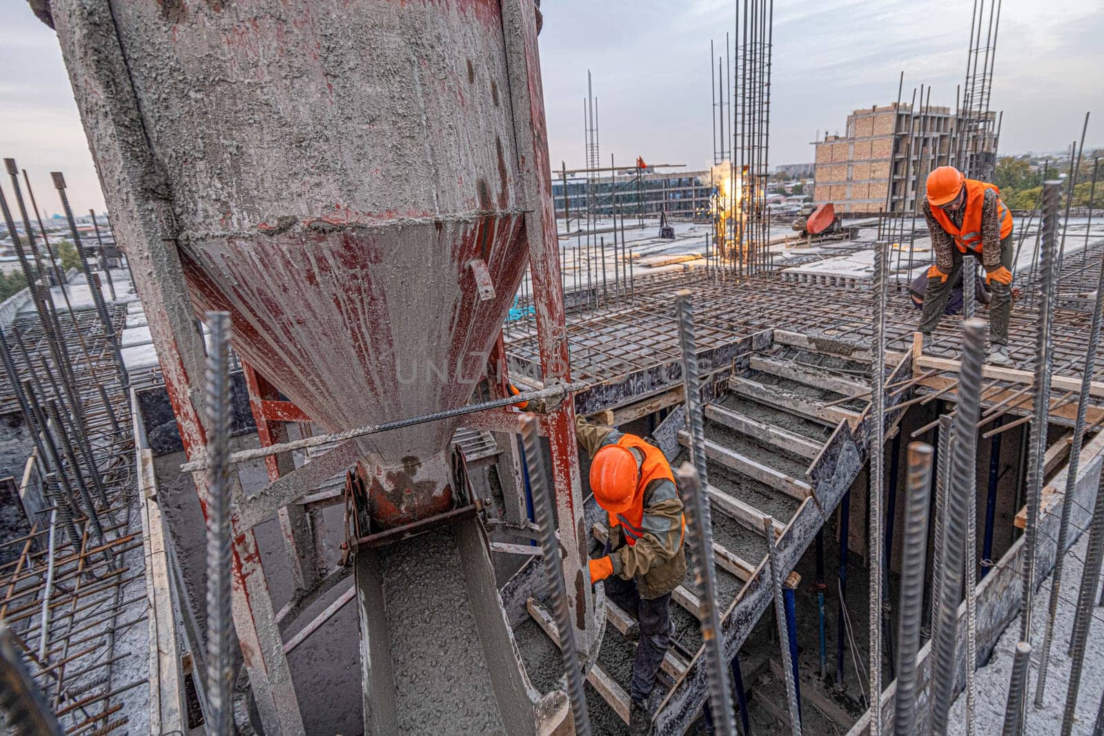 The workers on a building infrastructure roof with machinery and tools. Pouring concrete into a mold