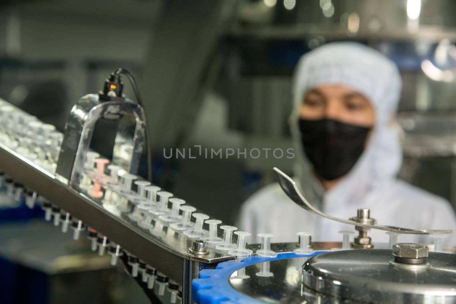 A closeup of the production of medical syringes with worker in a mask on blur background