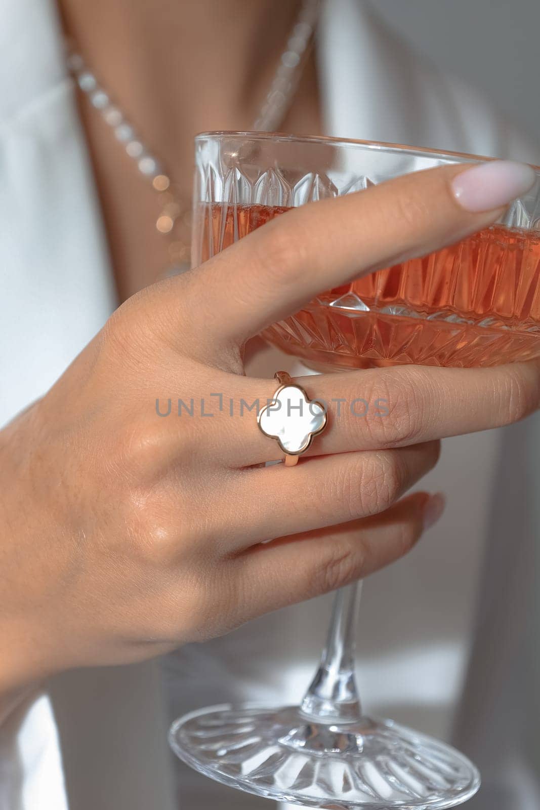 A vertical closeup shot of a Caucasian female hand holding a cocktail glass with a ring on the finger