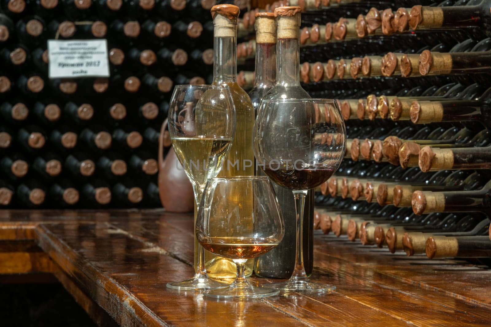 A closeup of bottles of different types of wine with a wine cellar in the background. Wine tasting