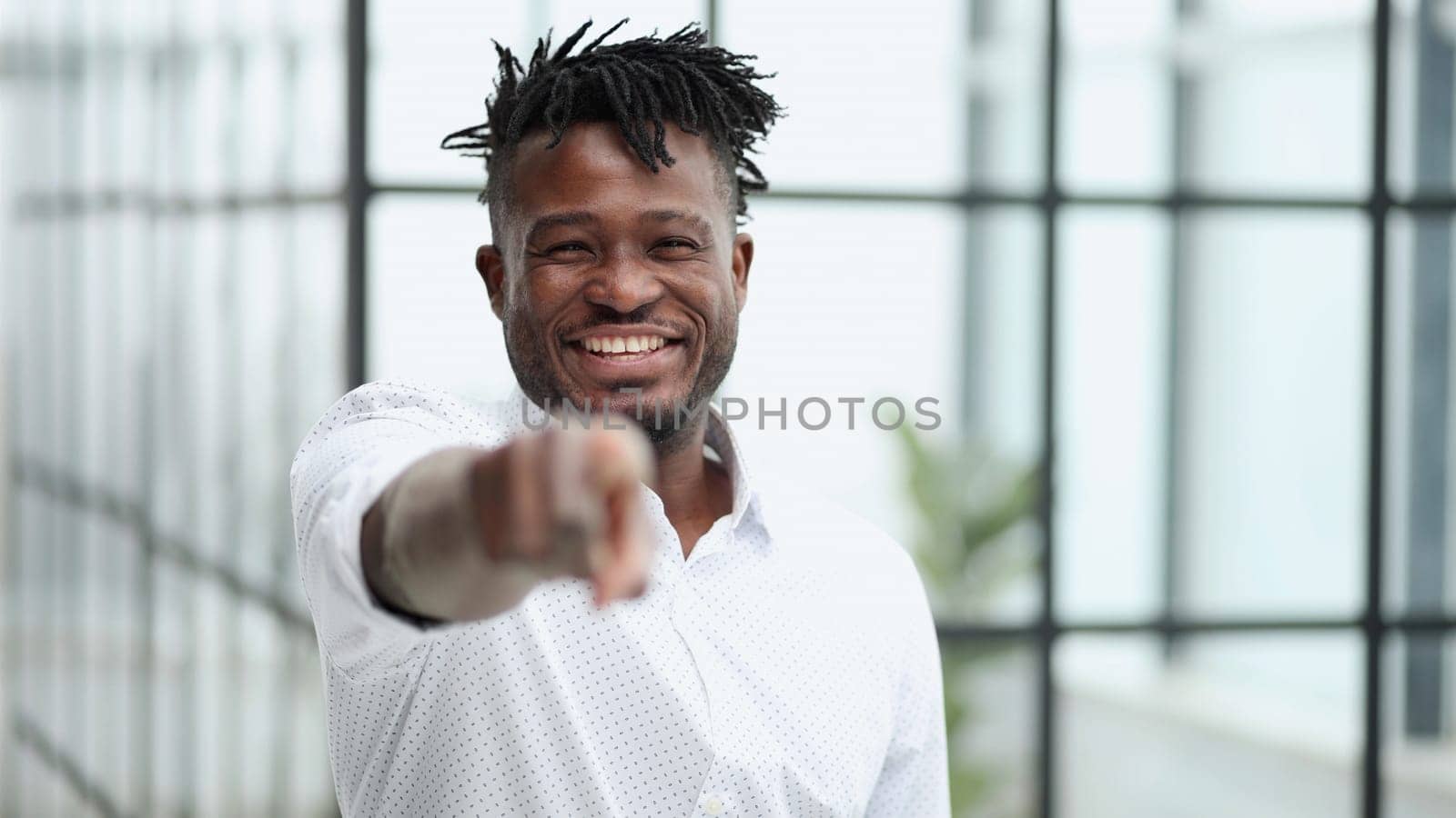Handsome happy young man in white shirt pointing at camera