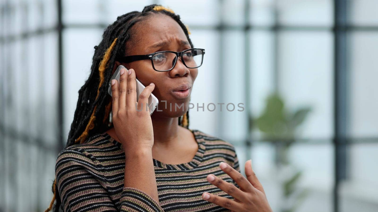 Close up portrait black woman employee in glasses working in office talking on mobile phone solving business issues distantly.