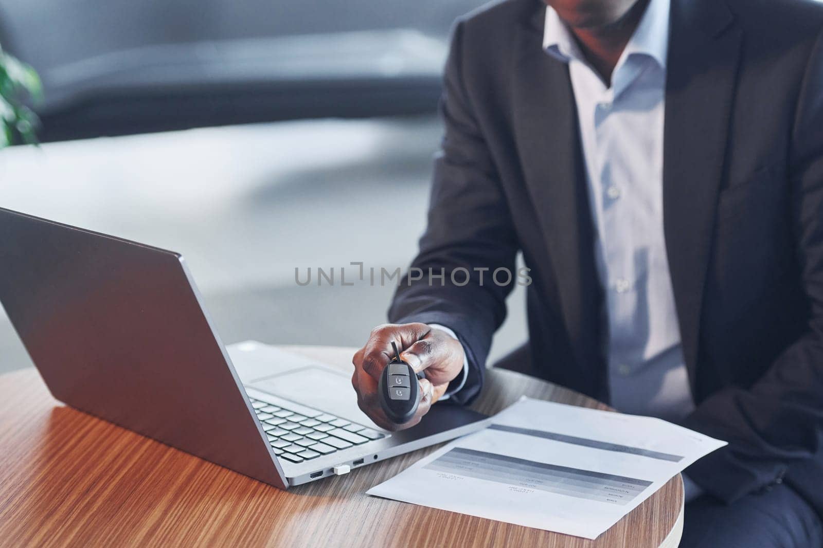 Office worker is sitting in autosalon by table with laptop.