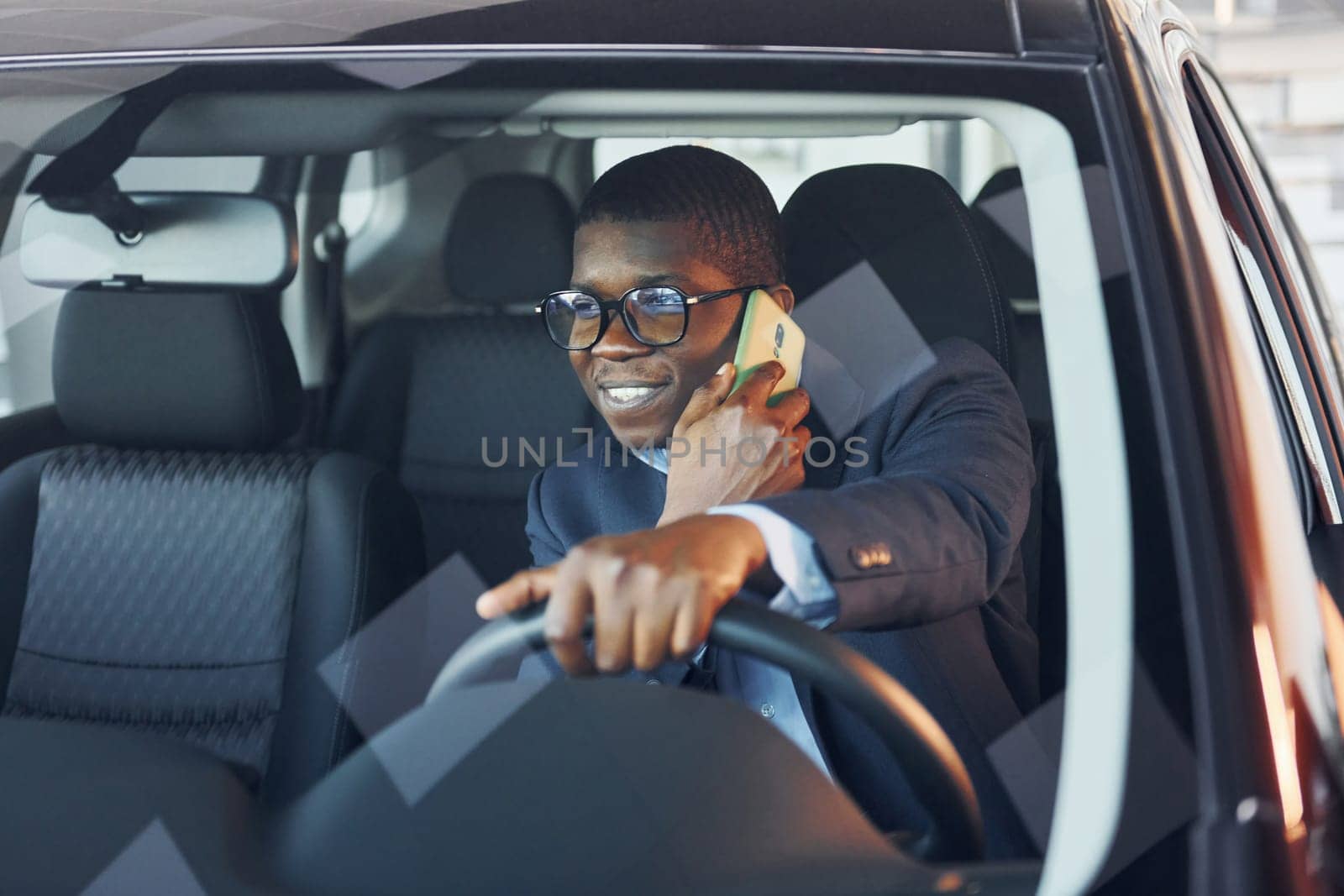 Front view. Young african american businessman in black suit is in the automobile.