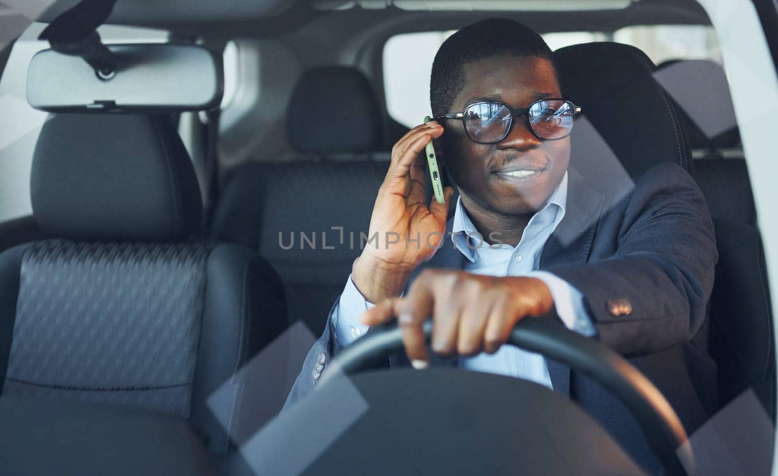Front view. Young african american businessman in black suit is in the automobile.
