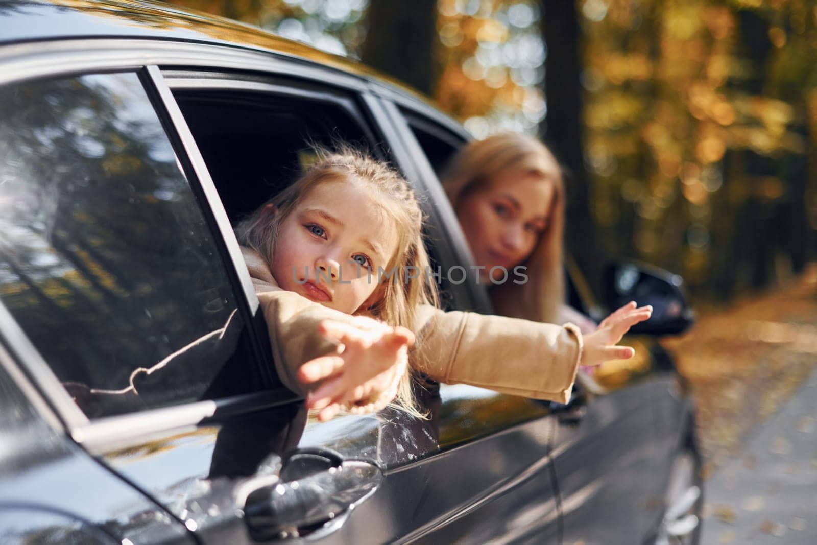 Little girl with her mother is sitting in the automobile and looking outside by Standret