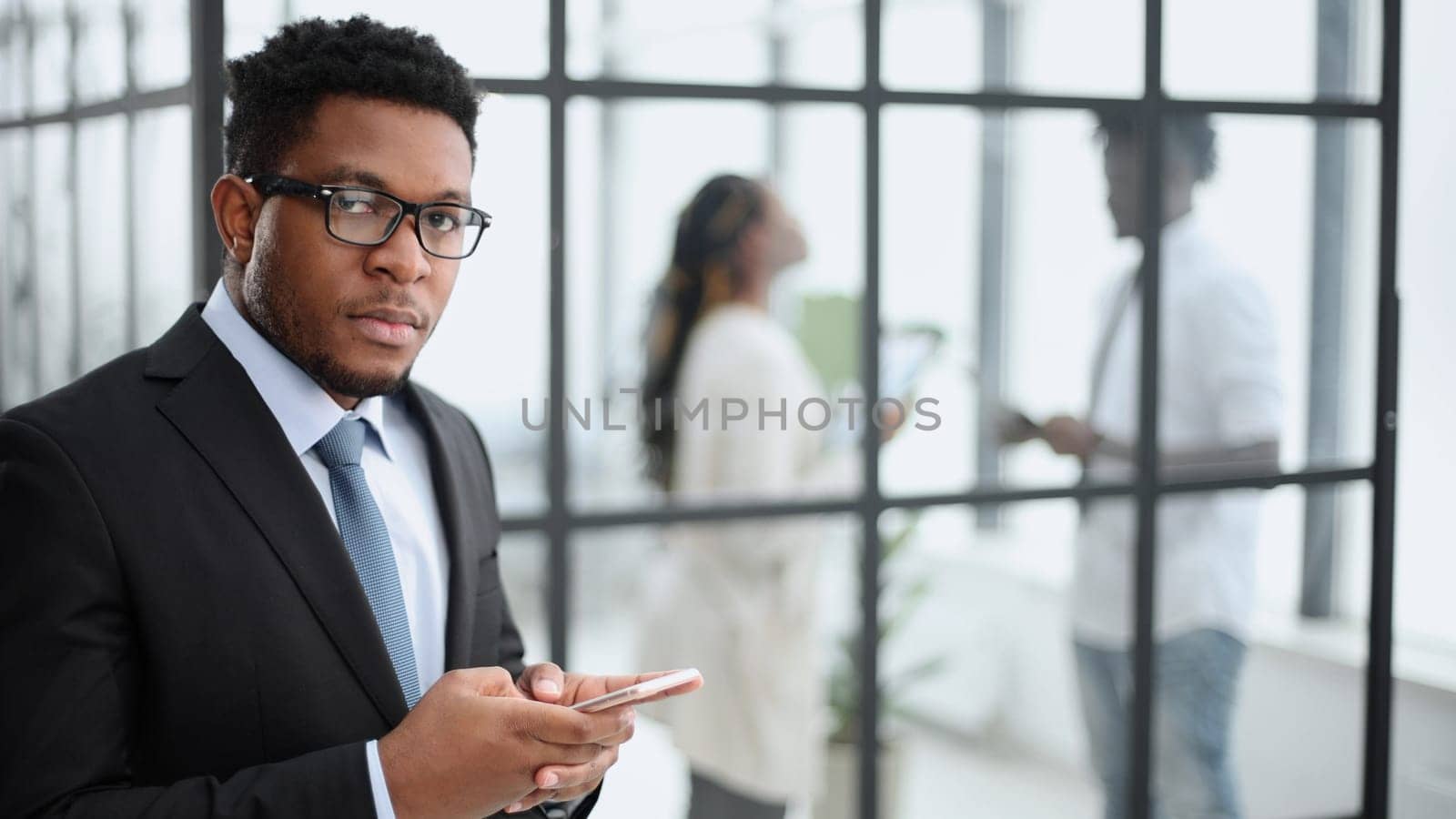 African American businessman in an elegant black suit looks at the camera against the background of colleagues
