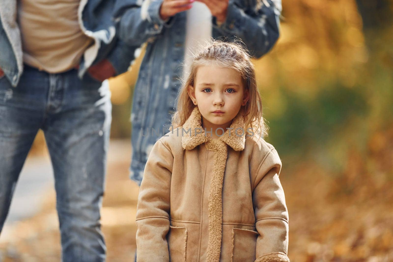 Little girl with her parents. Happy family is in the park at autumn time together.