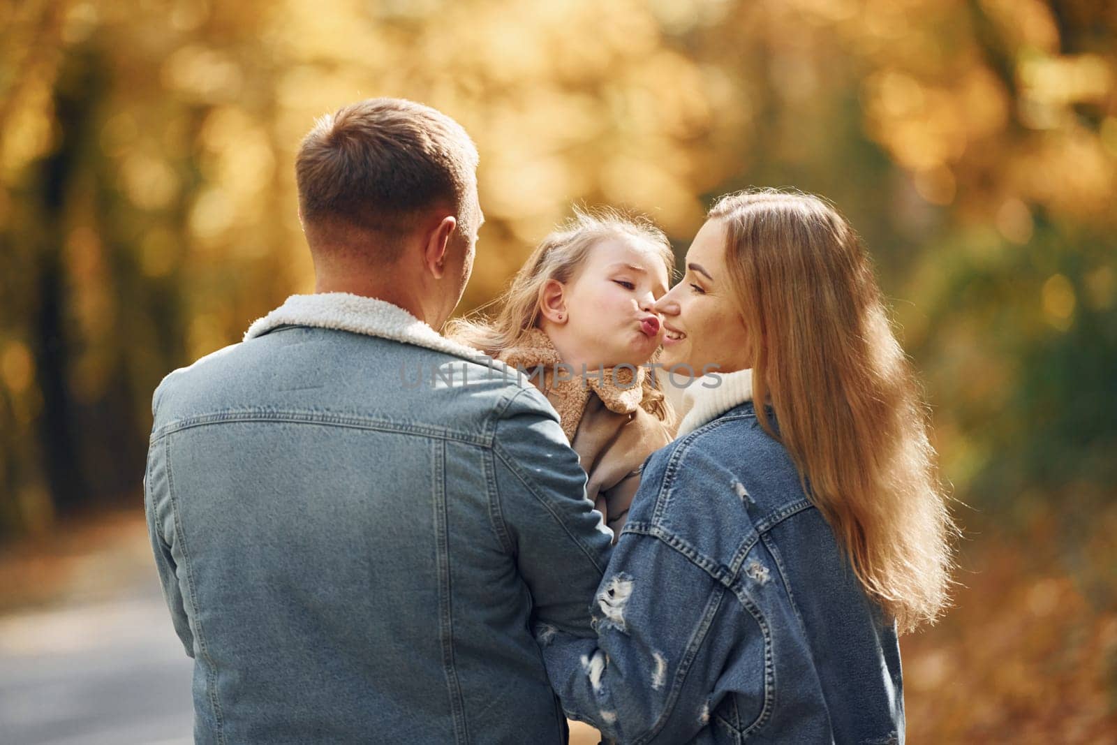Little girl with her parents. Happy family is in the park at autumn time together.