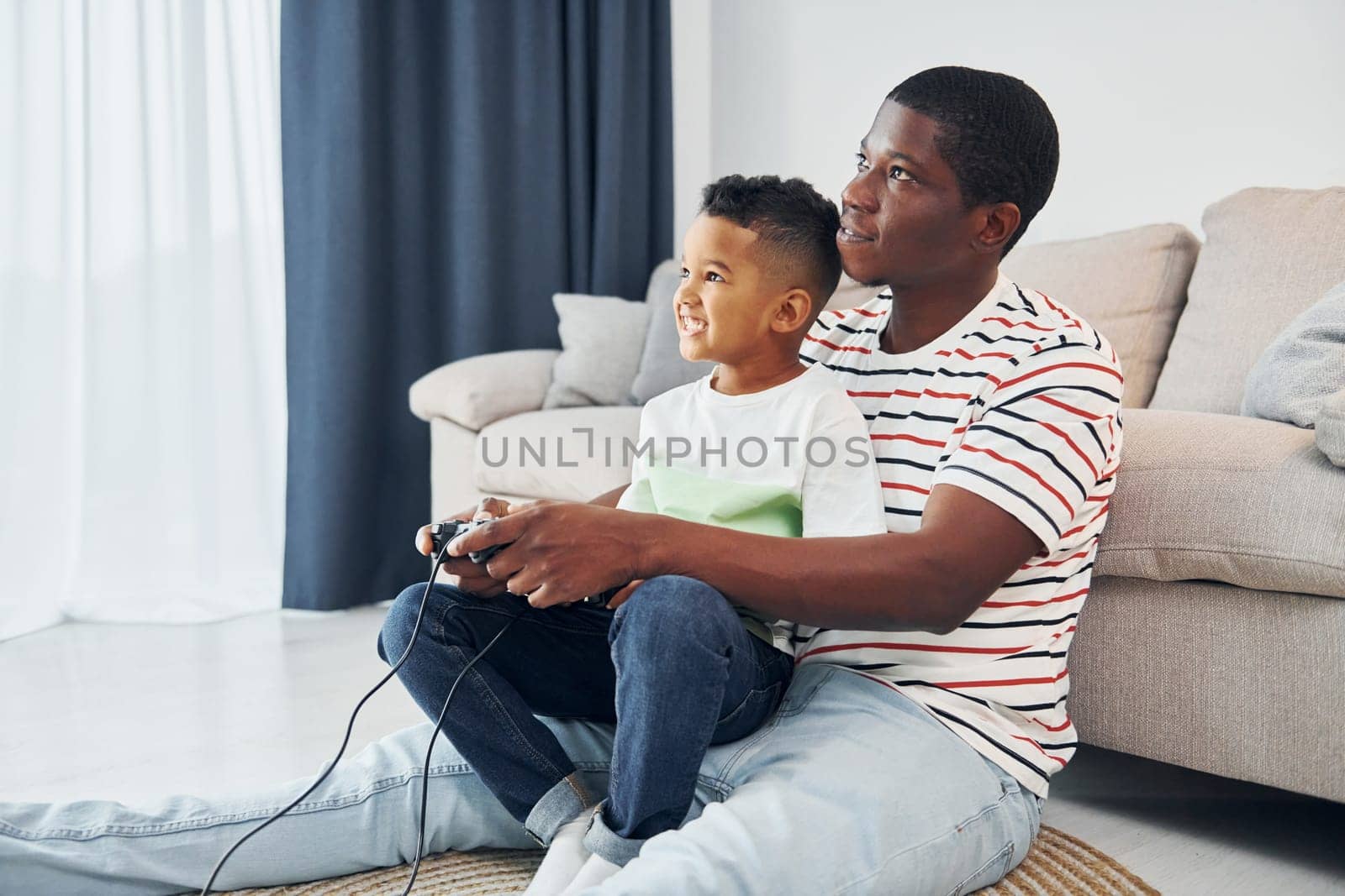 Playing video games. African american father with his young son at home.