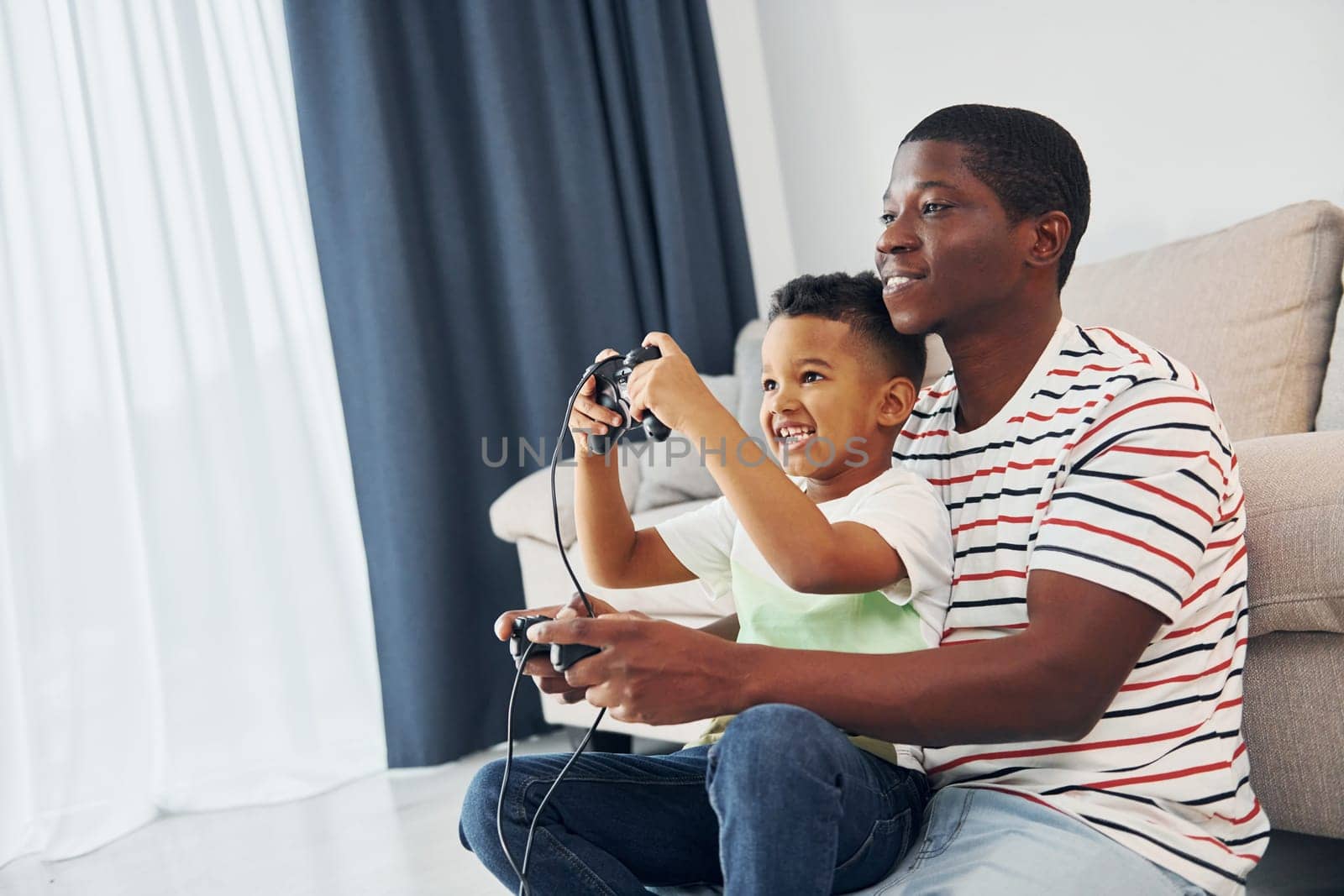Playing video games. African american father with his young son at home by Standret