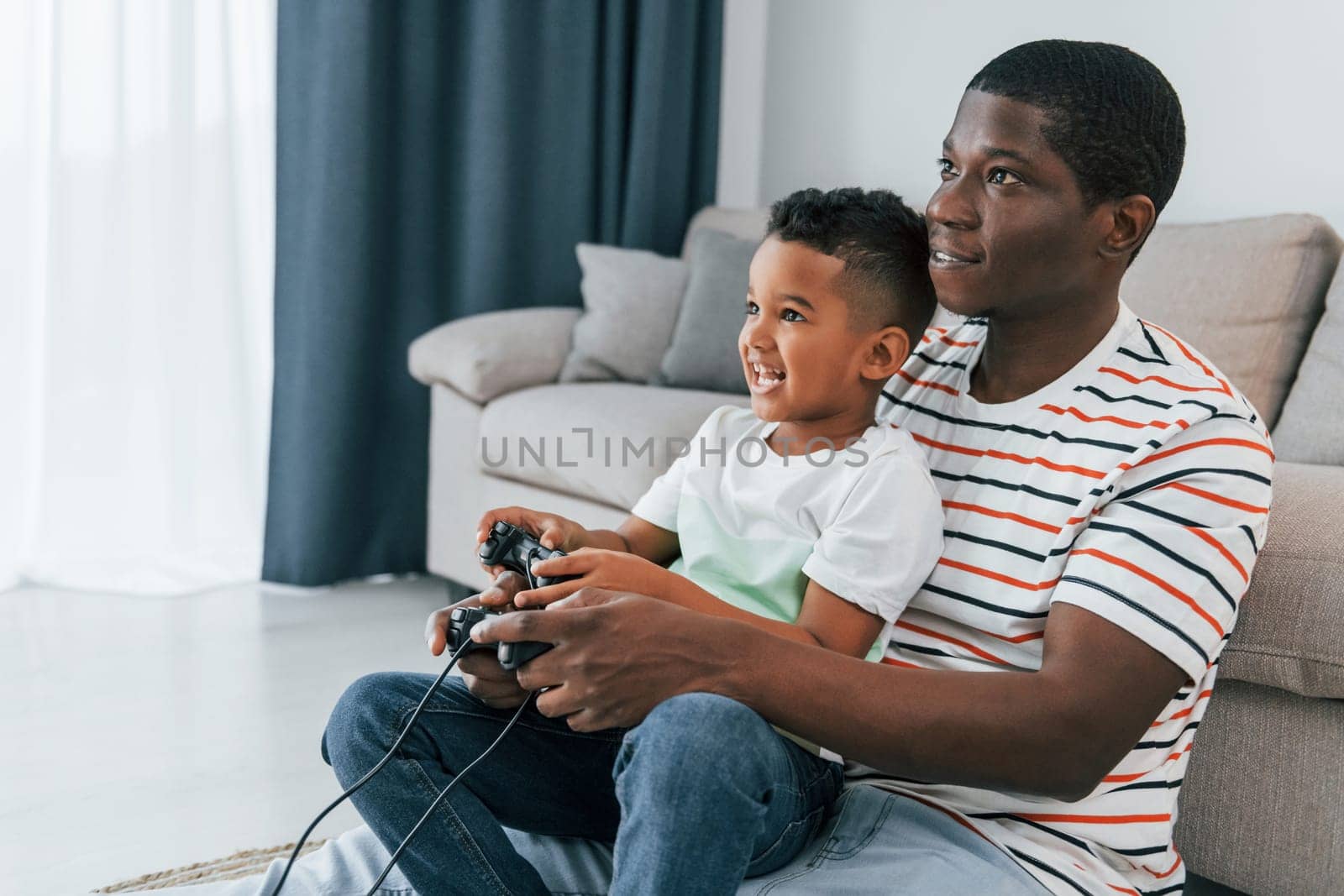 Using joysticks to play video game. African american father with his young son at home.