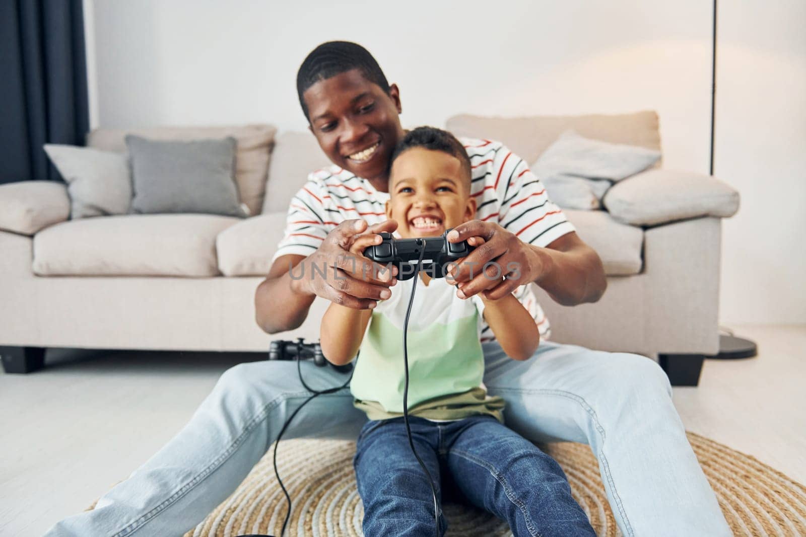 Using joysticks to play video game. African american father with his young son at home.