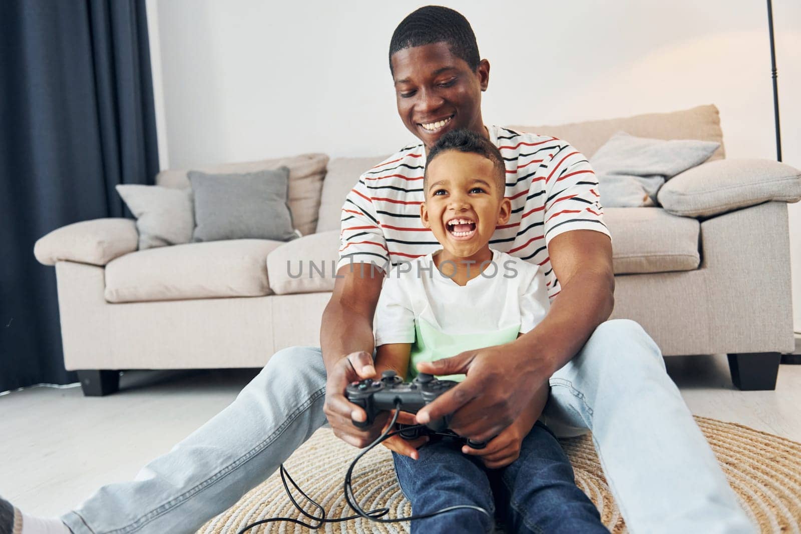 With joysticks in hands. African american father with his young son at home.