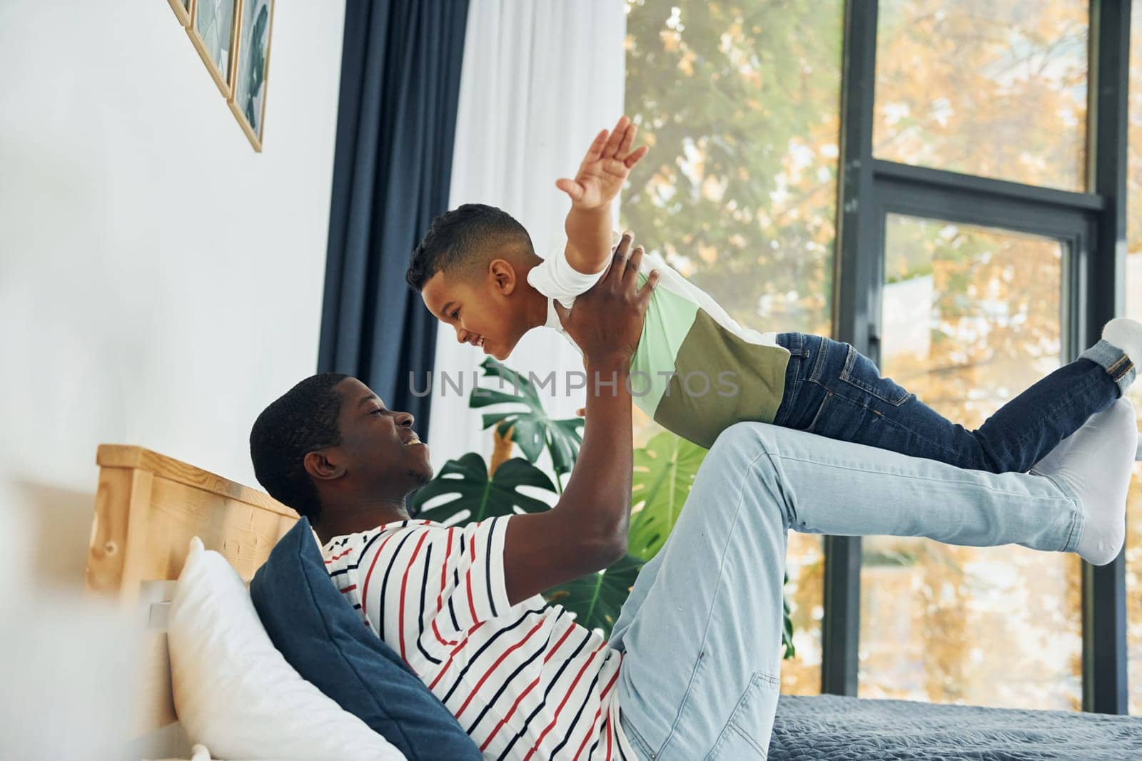 Laying down on the bed and having fun. African american father with his young son at home.