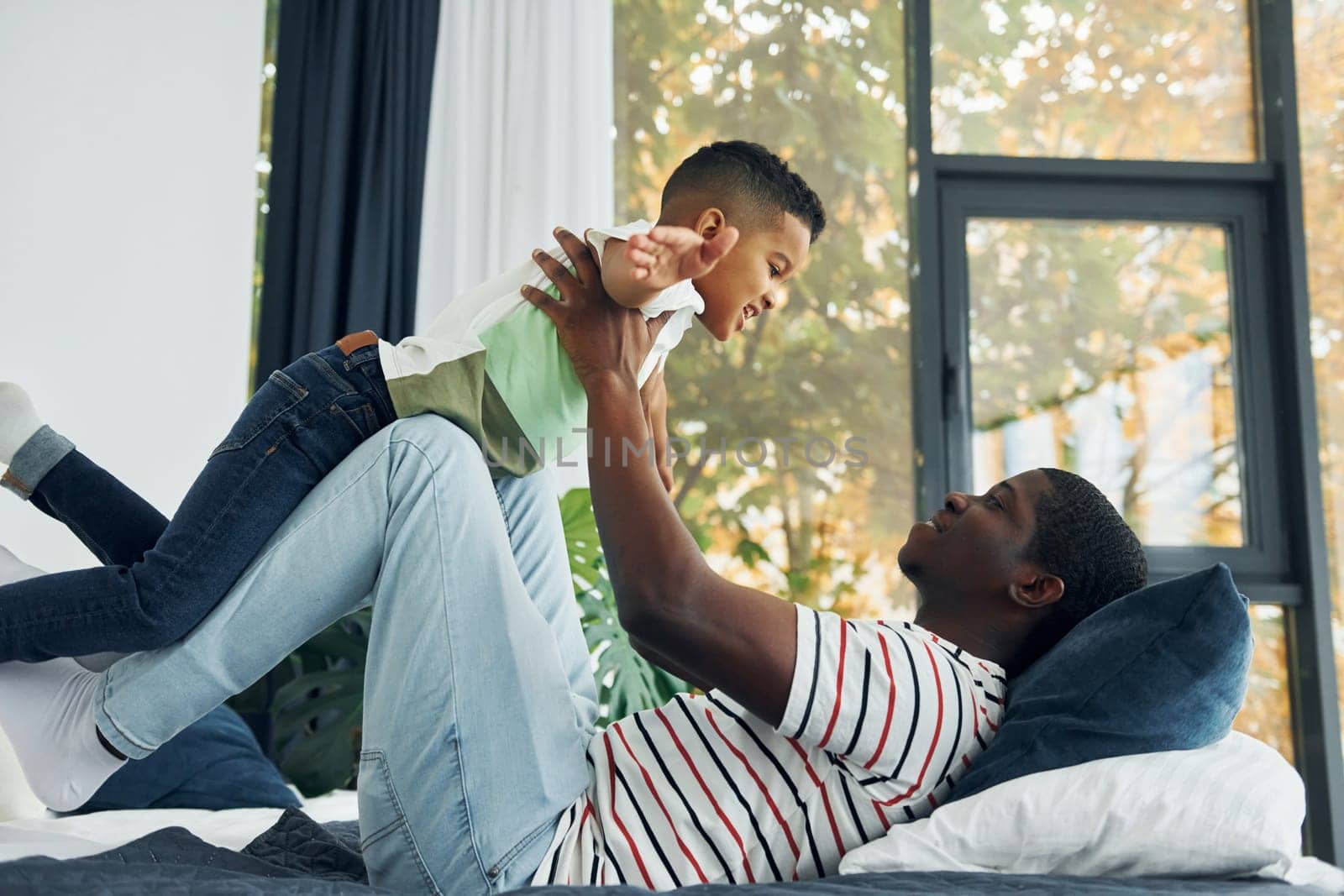 Laying down on the bed and having fun. African american father with his young son at home.