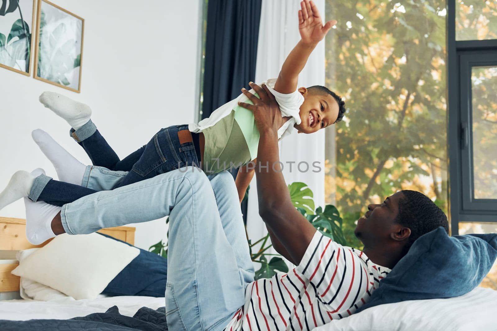 Laying down on the bed and having fun. African american father with his young son at home by Standret