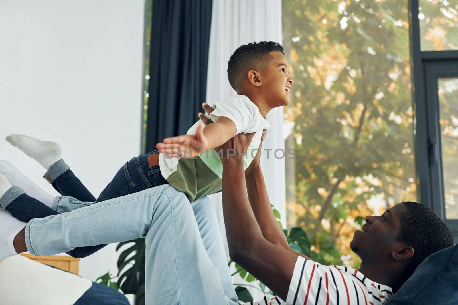 Laying down on the bed and having fun. African american father with his young son at home.