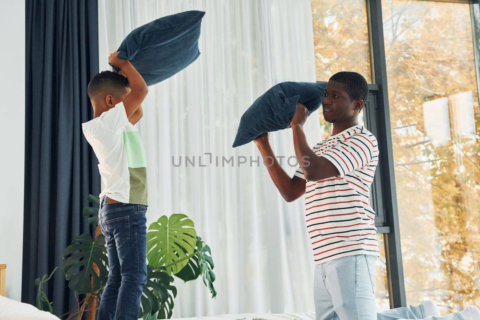 Pillow fight. African american father with his young son at home by Standret
