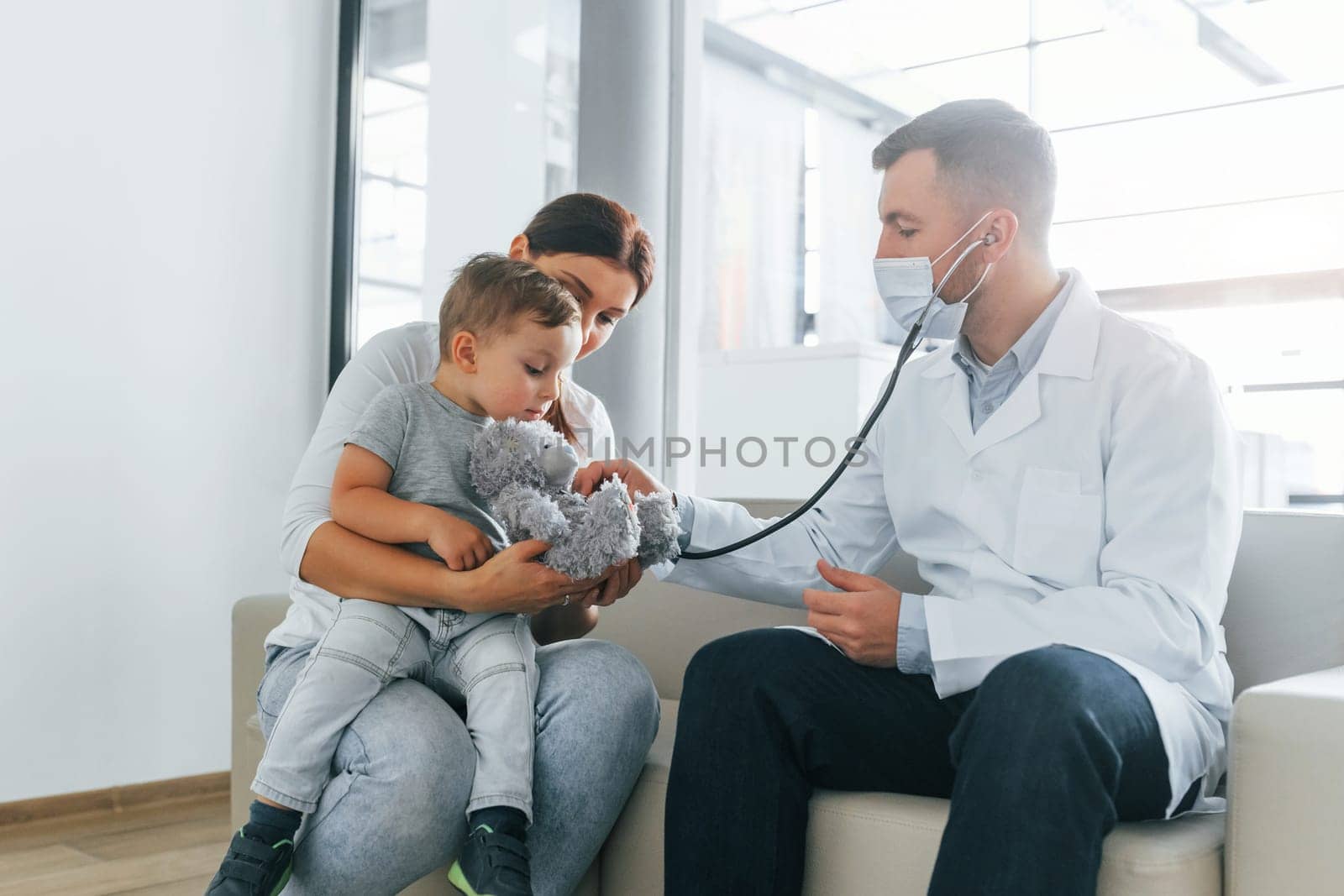 The little boy is being examined. Two doctors in white coats is in the clinic working together.
