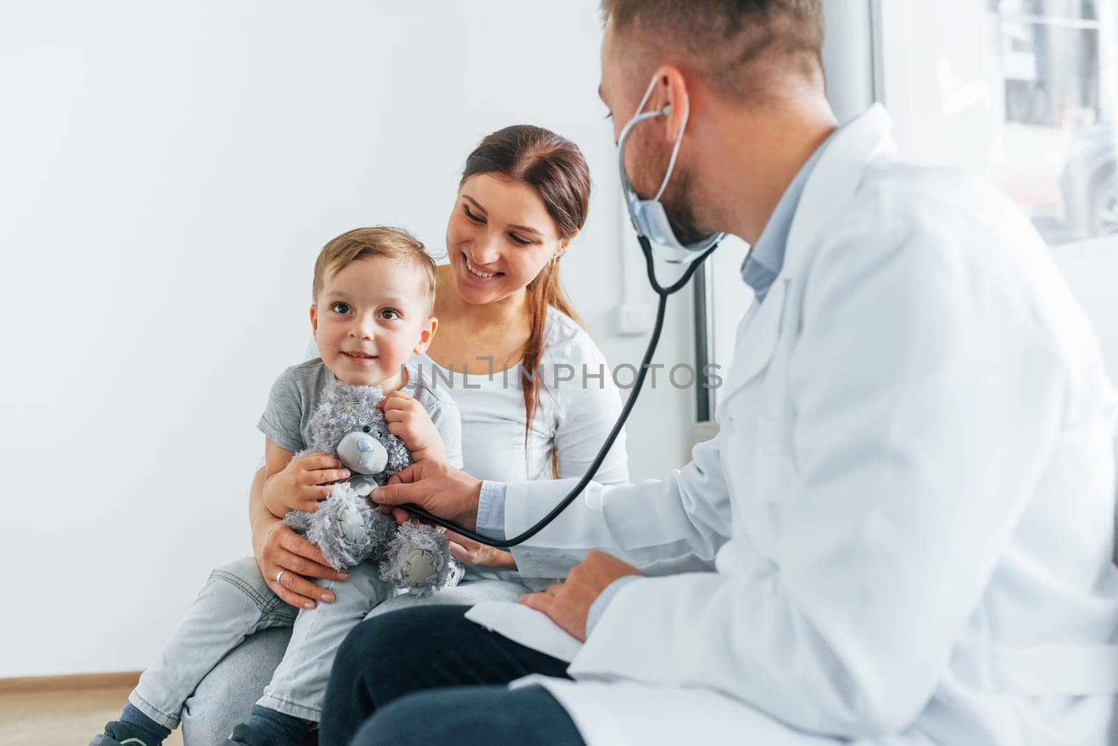 The little boy is being examined. Two doctors in white coats is in the clinic working together.