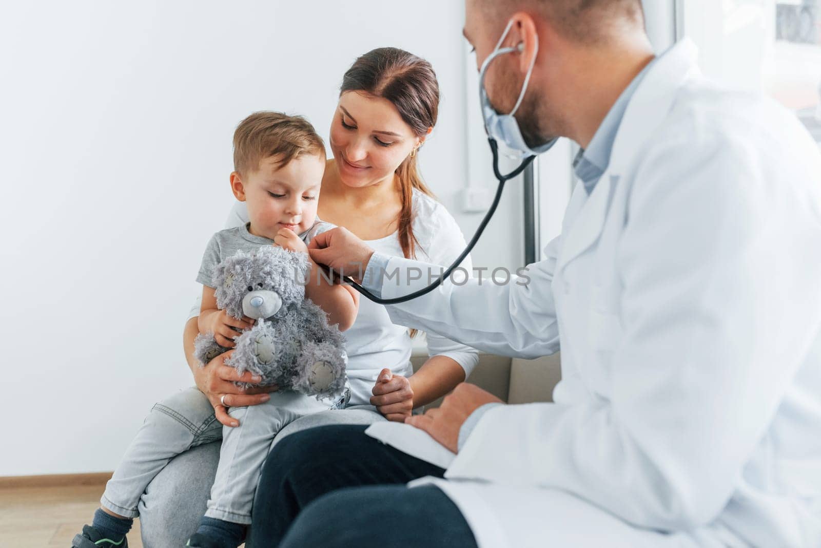 The little boy is being examined. Two doctors in white coats is in the clinic working together.