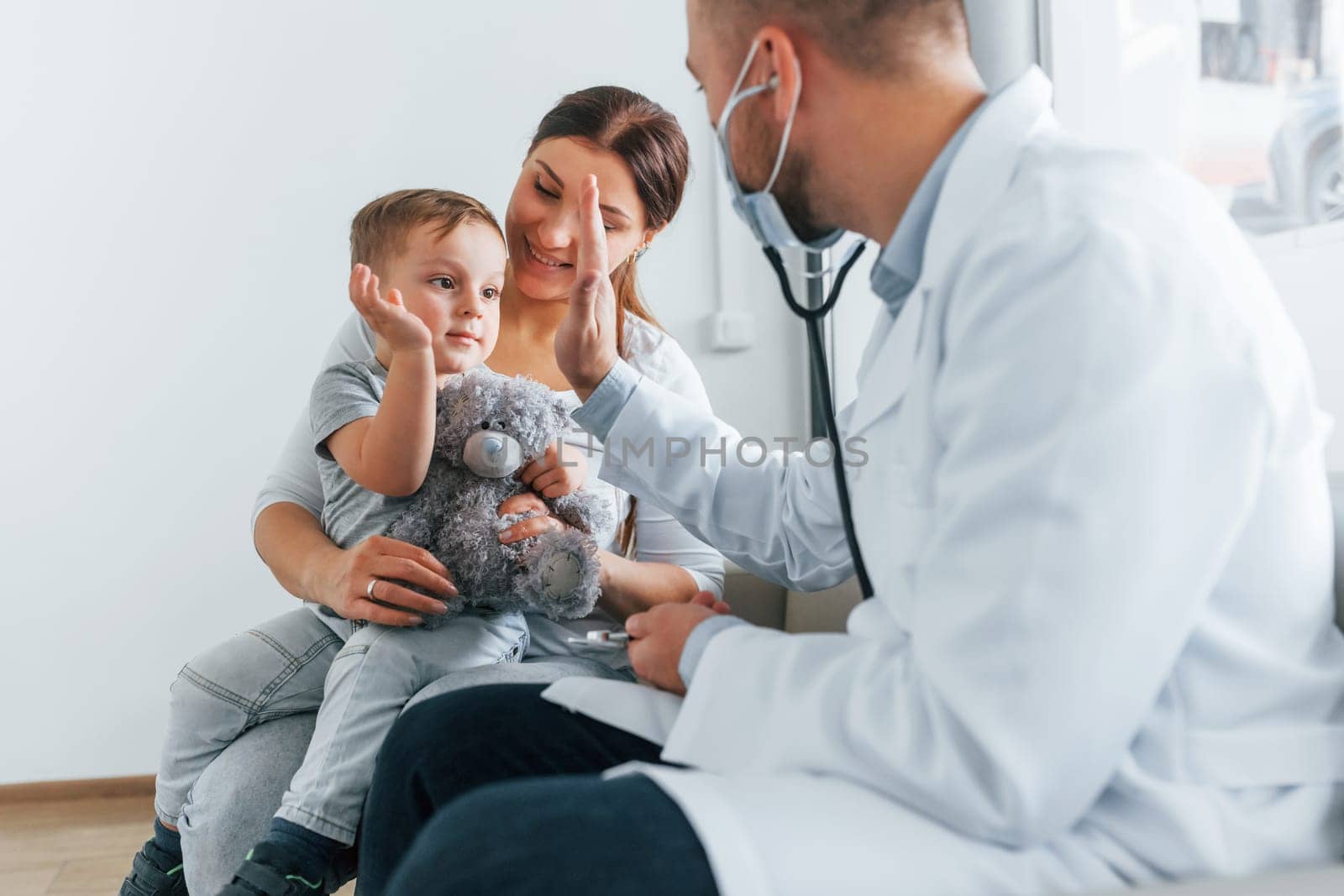 The little boy is being examined. Two doctors in white coats is in the clinic working together.