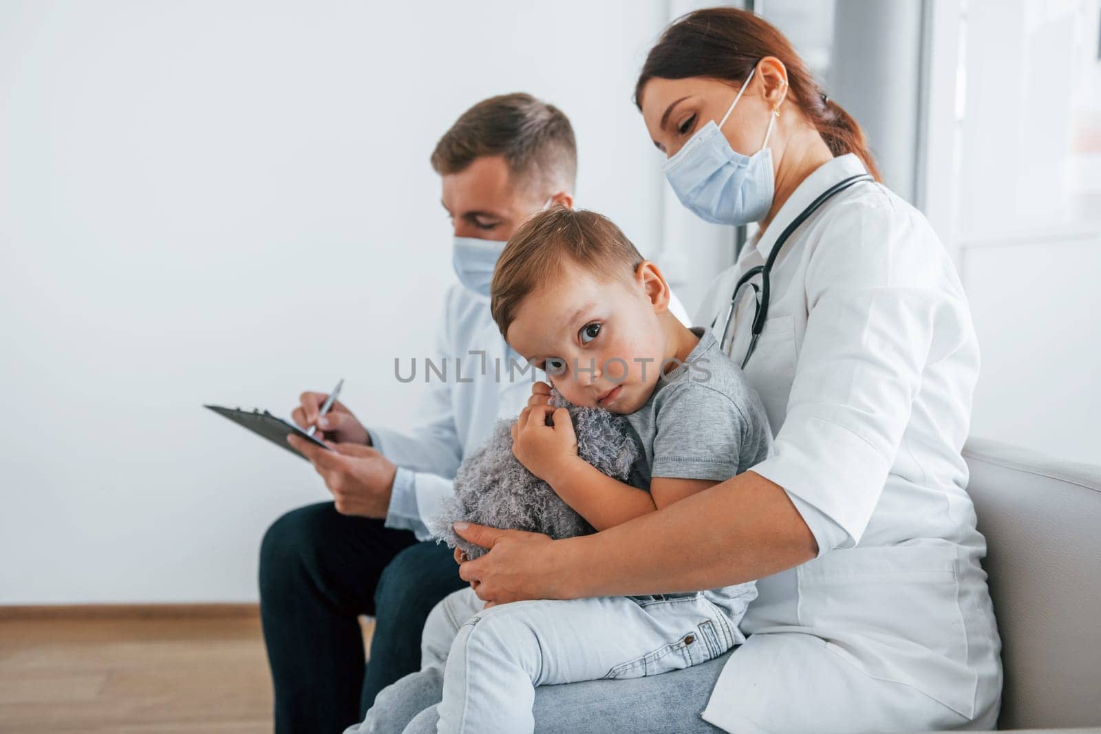Little boy is in the clinic. Two doctors in white coats is in the hospital working together.