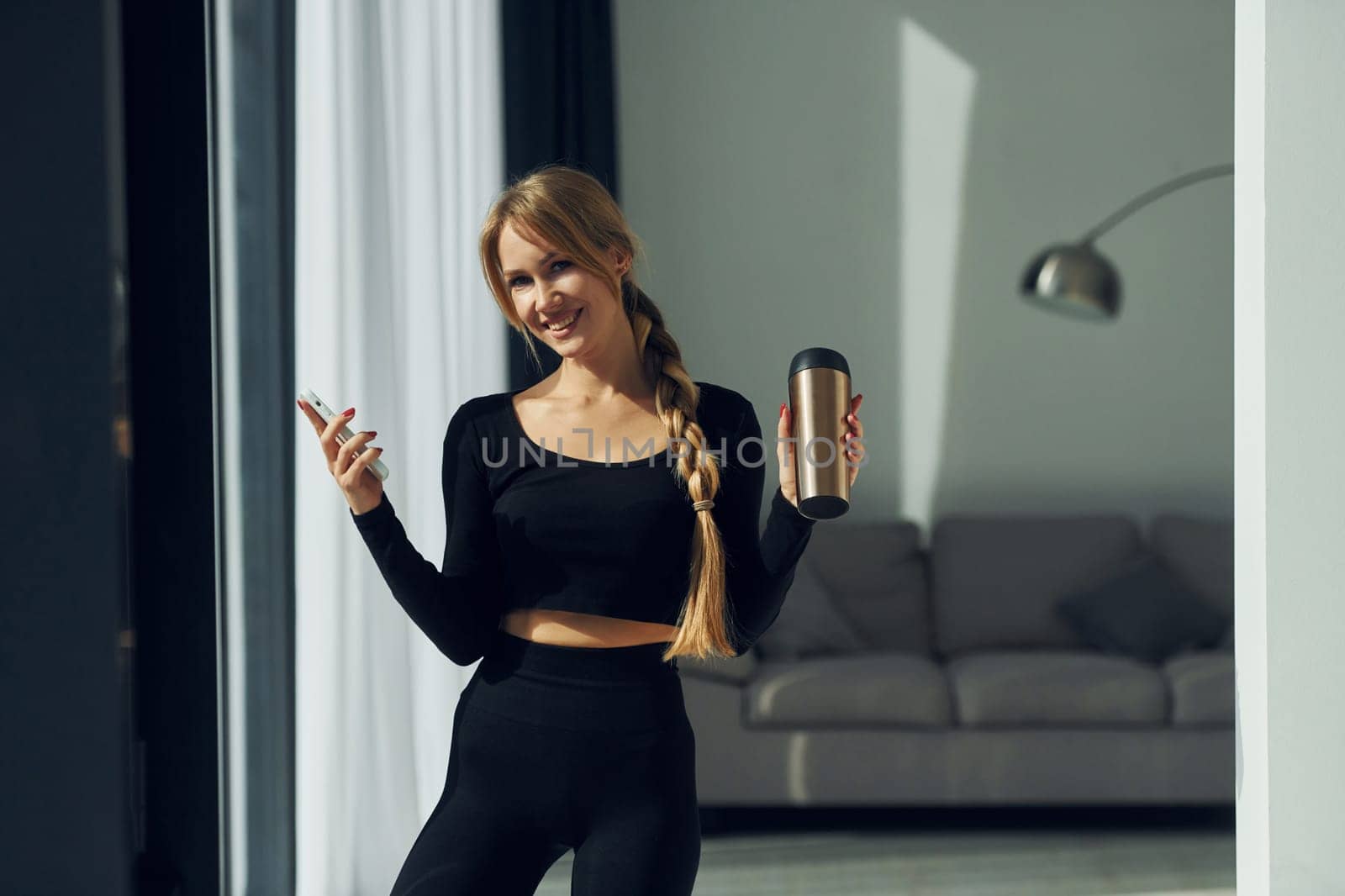 With phone in hands. Woman in sportive clothes doing yoga indoors.