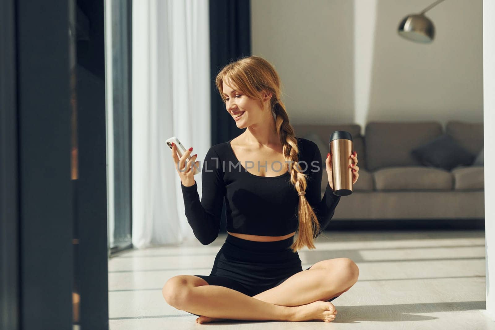 With phone in hands. Woman in sportive clothes doing yoga indoors.