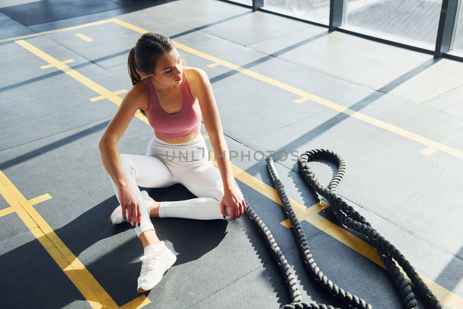 Sitting with rope. Beautiful young woman with slim body type is in the gym.