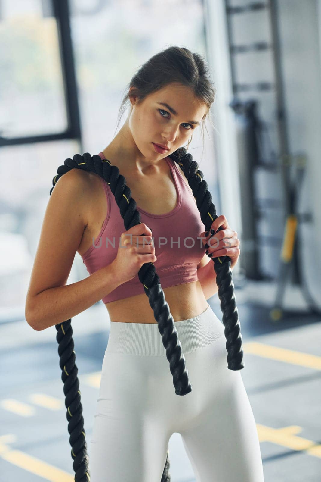 Standing and holding exercise equipment. Beautiful young woman with slim body type is in the gym.