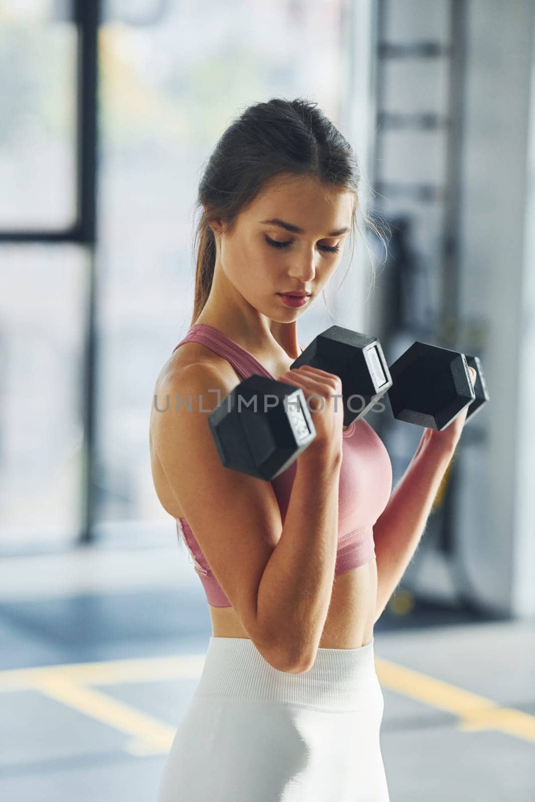 Holding dumbbells. Beautiful young woman with slim body type is in the gym.