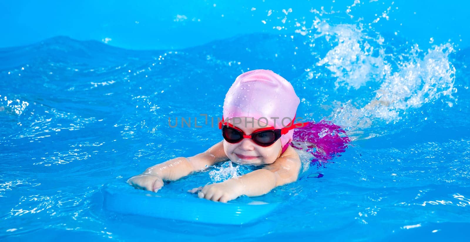 Little girl learning to swim in indoor pool with pool floating board