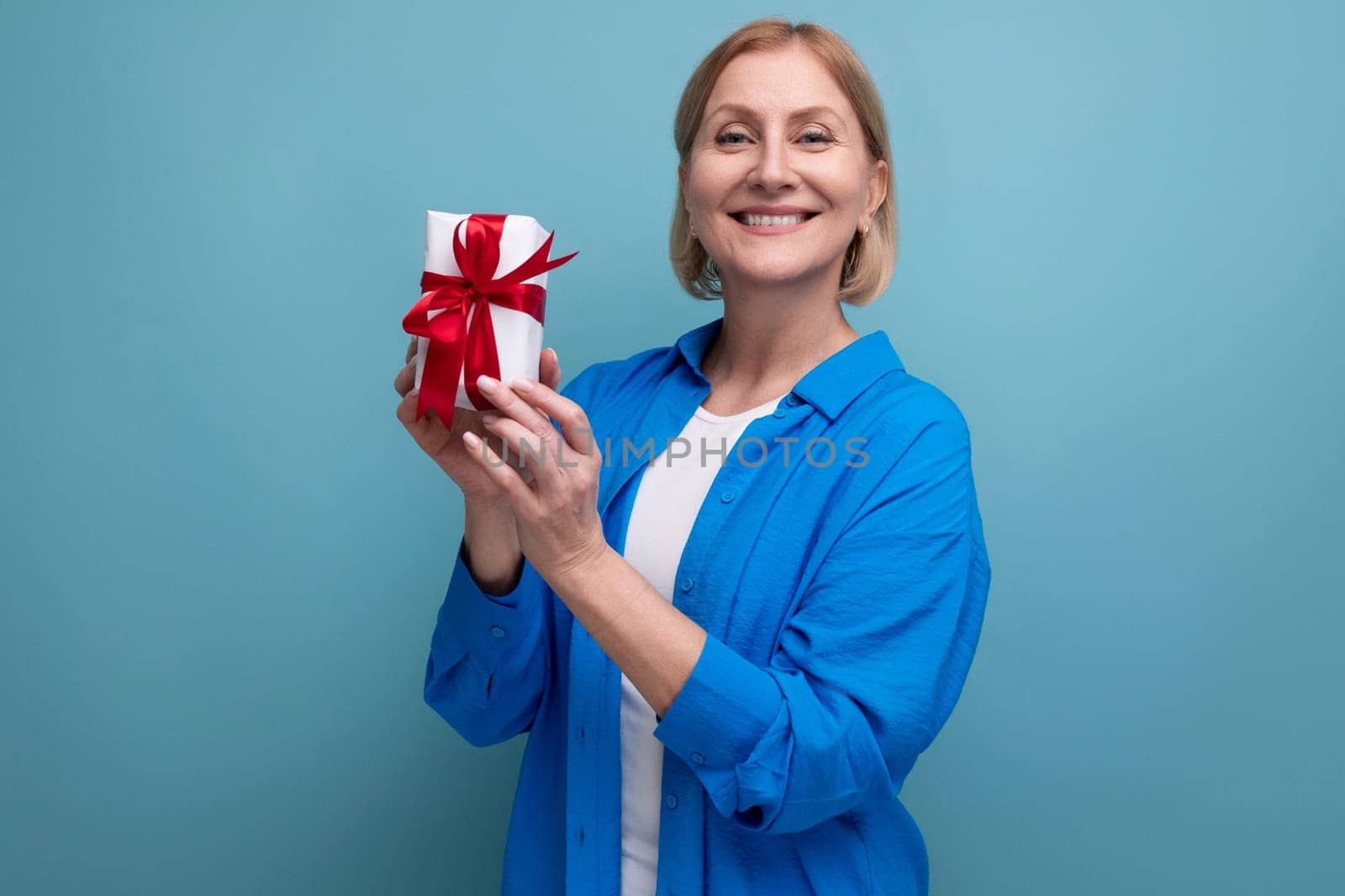 happy mature woman holding bonus gift on blue background copy space.